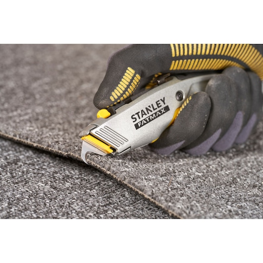 STANLEY 0-10-789 utility knife cutting carpet, close-up, grey and yellow handle.