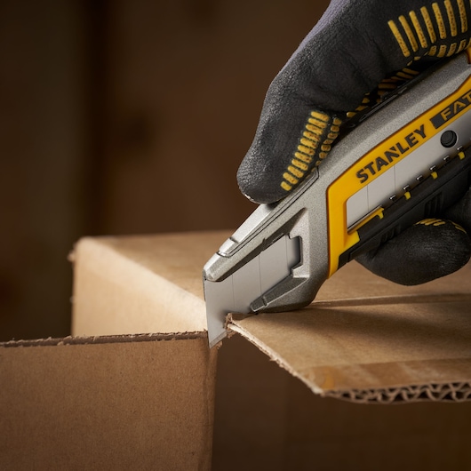 Photo of STANLEY 0-11-301 utility knife cutting cardboard, close-up view with gloved hand.