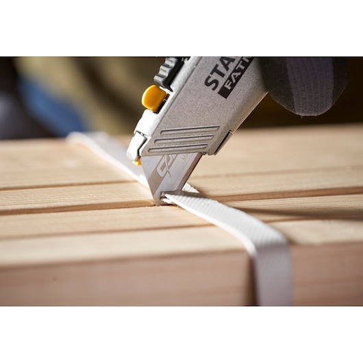 STANLEY 0-11-800 utility knife cutting white strap on wooden surface, close-up angle.