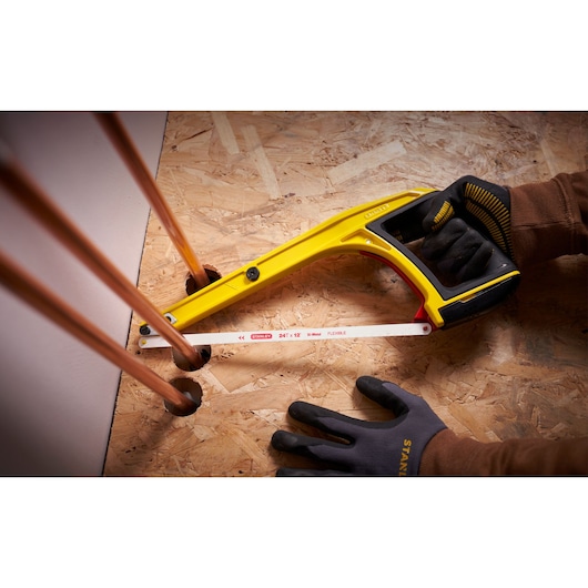 Photo of STANLEY 0-20-108 hacksaw with yellow frame cutting copper pipe, shown in a work glove hand.