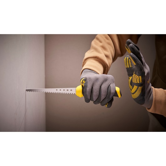 Photo of STANLEY 0-20-556 drywall saw used by gloved hands for cutting plasterboard, side angle.