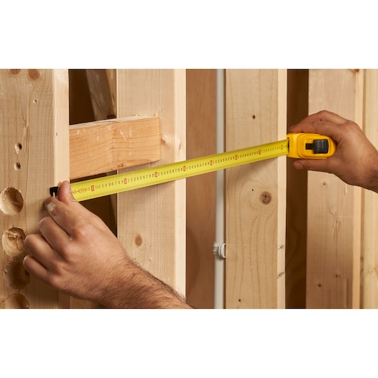 Photo of STANLEY 0-30-457 tape measure in use, measuring distance between wooden studs, close-up angle.