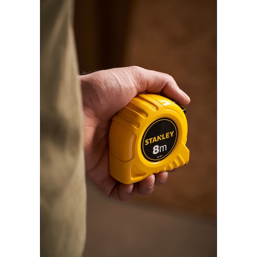 Photo of STANLEY 0-30-457 yellow 8m tape measure held in a hand, product photography.