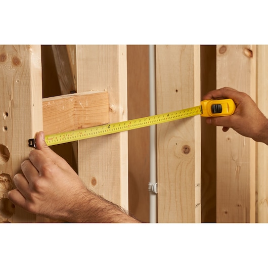 STANLEY 0-30-496 tape measure in use measuring wooden studs, product photography.