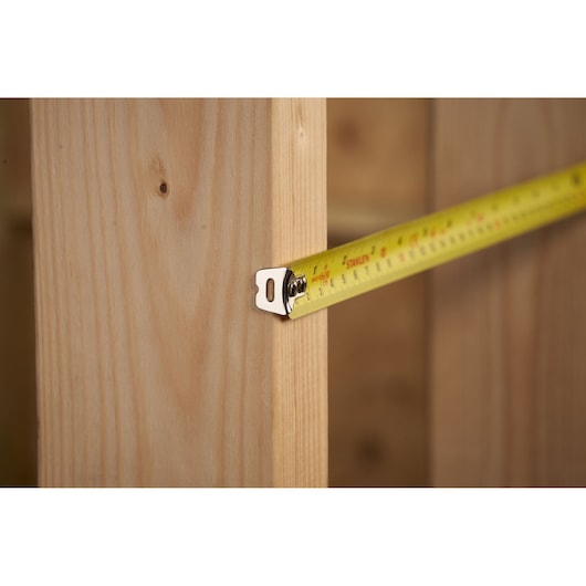STANLEY 0-30-496 tape measure extending to measure wooden stud, close-up photography.