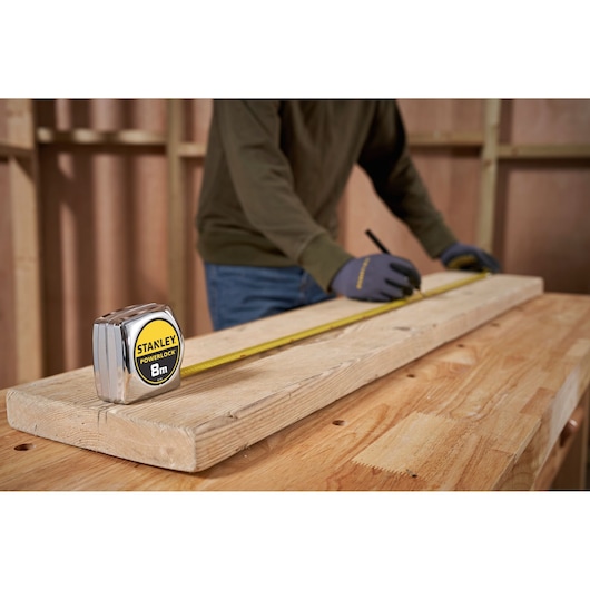 Stanley 0-33-198 tape measure on wood plank, worker marking length, workshop setting.