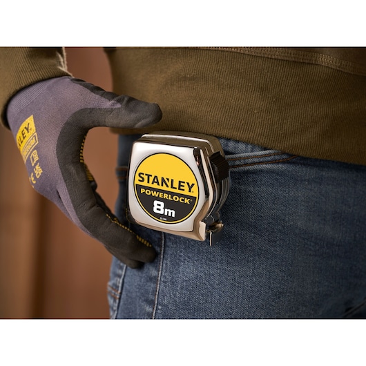 STANLEY 0-33-198 PowerLock 8m tape measure on denim belt, gloved hand holding the case.