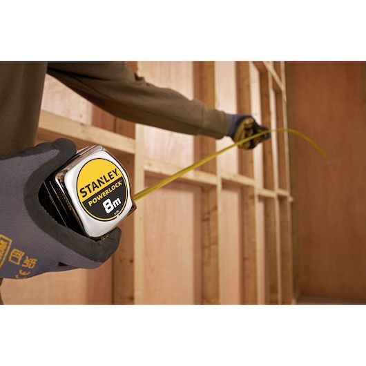Photo of STANLEY 0-33-198 PowerLock tape measure held by gloved hand, measuring wooden wall frame.