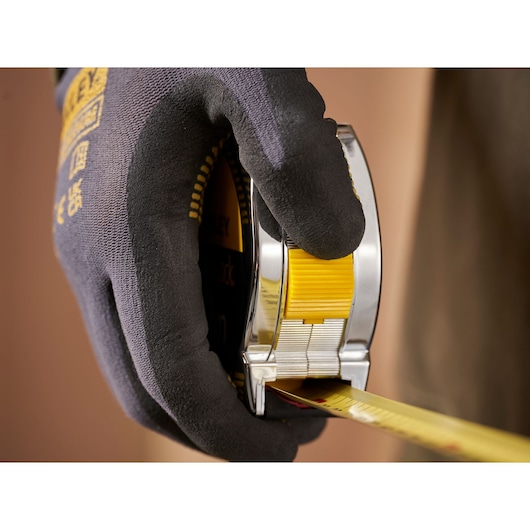 Close-up photo of STANLEY 0-33-442 tape measure held in gloved hand, showing yellow tape being extended.
