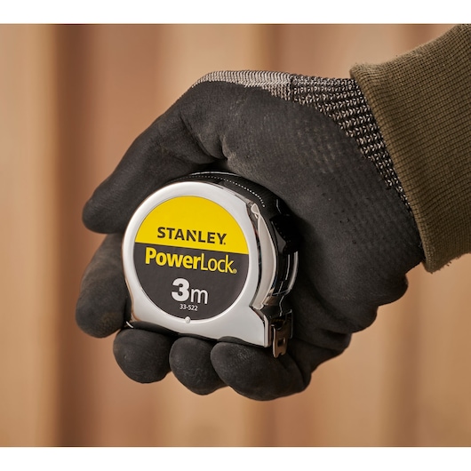 Photo of STANLEY 0-33-522 PowerLock 3m tape measure held in gloved hand, close-up view.