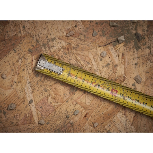 STANLEY 0-33-532 yellow tape measure on wood board with scattered stones, close-up view.