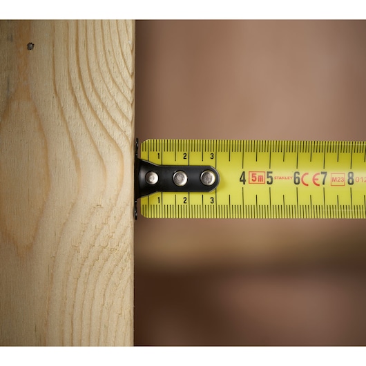 STANLEY 0-33-720 tape measure yellow blade measuring wooden plank, close-up side angle.