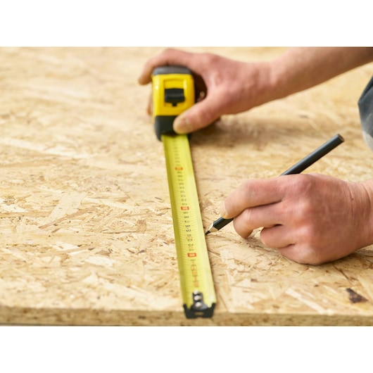 Photo of STANLEY 0-33-728 tape measure marking measurements on plywood, close-up angle.
