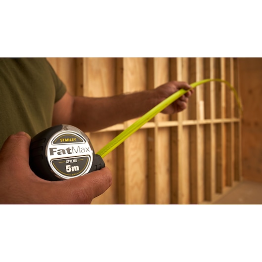 STANLEY 0-33-887 tape measure being used to measure wooden studs, close-up side view.