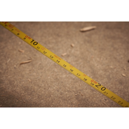 STANLEY 0-34-108 yellow tape measure with metric markings, close-up side view on sandy surface.