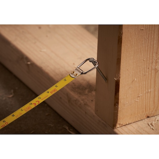 STANLEY 0-34-134 tape measure hooked on a nail in wooden framing, close-up side angle.