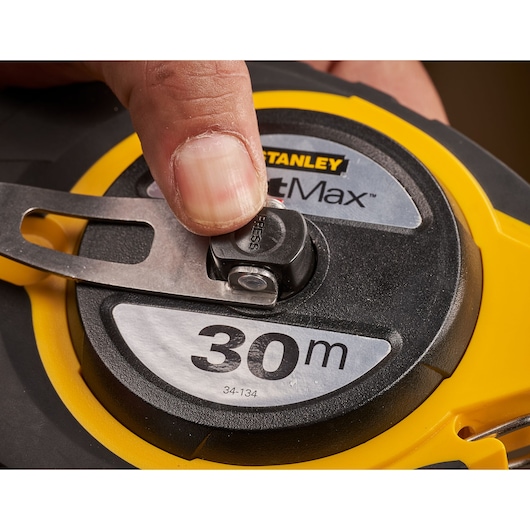 Photo of STANLEY 0-34-134 tape measure, close-up on the reel and hand pressing release button, 30 meter length shown.