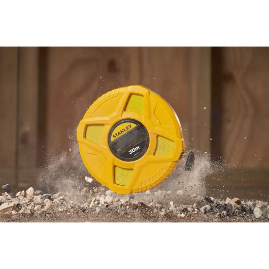 STANLEY 0-34-297 yellow 30m measuring tape reel on construction debris, product category photography.