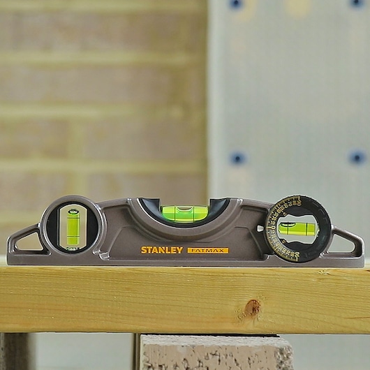 STANLEY 0-43-609 photography of brown torpedo level with three vials, shown on a wooden plank, front angle.