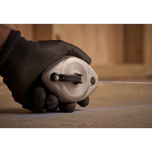 Photo of STANLEY 0-47-100 chalk line reel held in a gloved hand on a concrete surface.