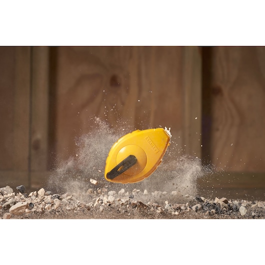 STANLEY 0-47-440 chalk line reel in yellow, dynamic action on dirt and rocks, photography product shot.