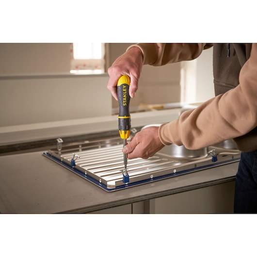Stanley 0-68-010 screwdriver used to attach metal panel on countertop, close-up photography.