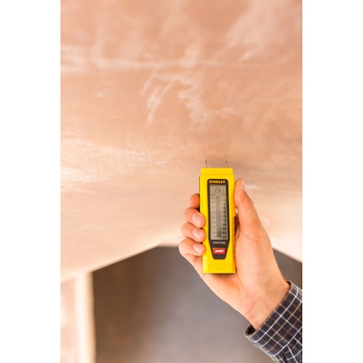 Photo of STANLEY 0-77-030 moisture meter used on plaster wall, held in hand.