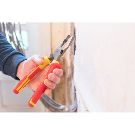 STANLEY 0-84-002 insulated pliers with red and yellow handles, held near a wall, product photography.