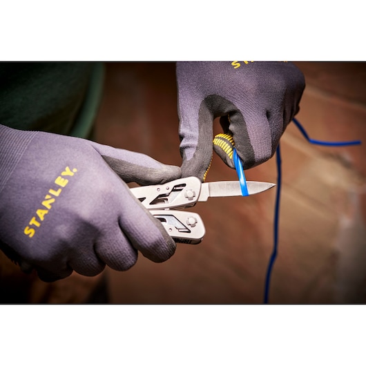 STANLEY 0-84-519 multitool blade cutting blue wire, close-up, worn with STANLEY gloves.