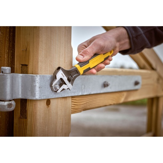 Stanley 0-90-949 adjustable wrench tightening a bolt on a metal hinge attached to a wooden gate, close-up.