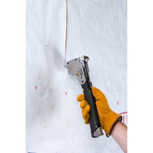 Photo of STANLEY 0-PHT350 staple hammer being used by a gloved hand to fasten material to a wall.