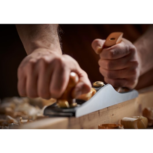 STANLEY 1-12-137 hand plane shaving wood, close-up of hands using tool, wood shavings visible.
