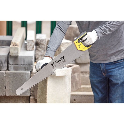 Photo of STANLEY 1-15-441 hand saw cutting a concrete block, yellow handle, construction context.