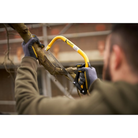 Stanley 1-20-447 bow saw cutting tree branch, yellow frame, outdoor setting.