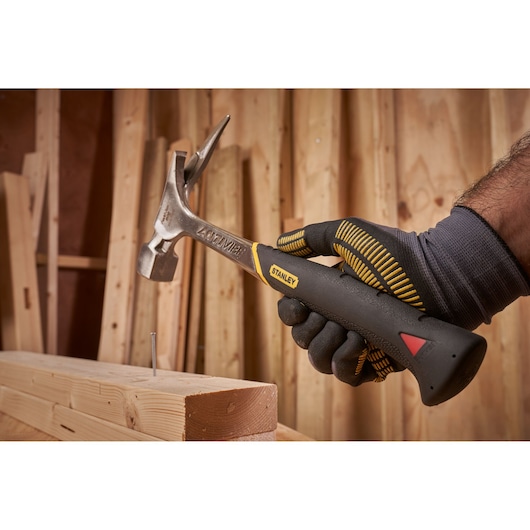 STANLEY 1-51-937 claw hammer in gloved hand, driving nail into wood, workshop background.