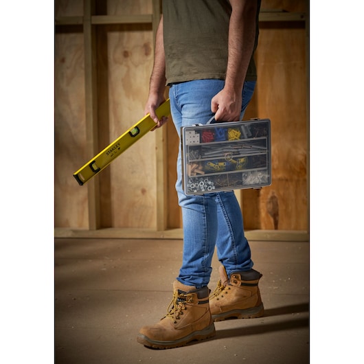 STANLEY 1-92-761 hardware organizer case held by person wearing tan work boots in construction setting.