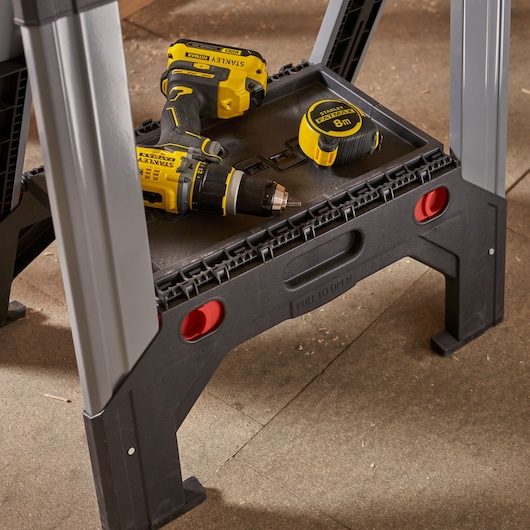 STANLEY 1-92-980 black and gray sawhorse with a yellow STANLEY tape measure and drill on the shelf, angled view.