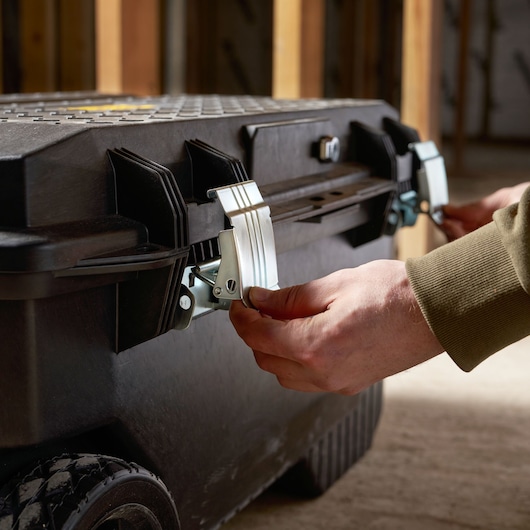 STANLEY 1-94-850 tool chest close-up, hands unlocking metal latches, black rugged exterior, photography