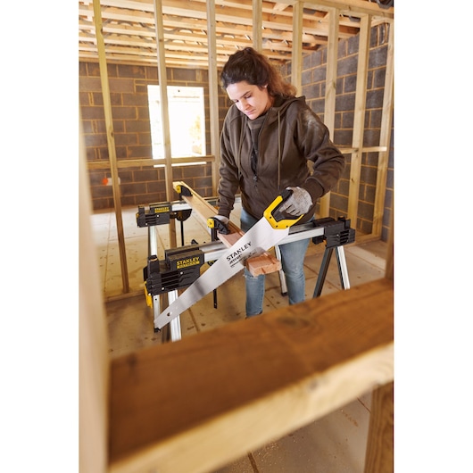 Photo of STANLEY 2-15-244 hand saw in use, cutting wood on sawhorse at construction site.