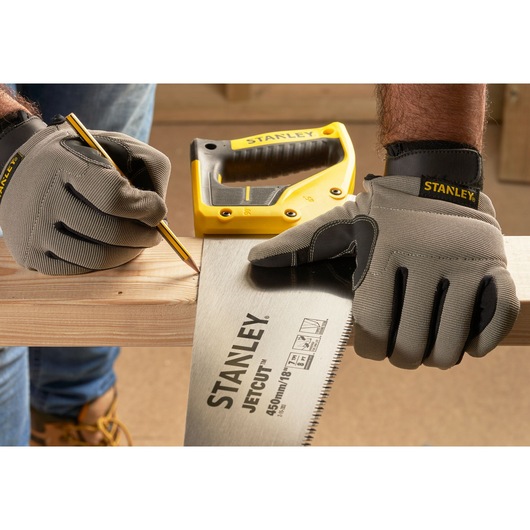 STANLEY 2-15-283 hand saw with yellow handle held by gloved hands, marking wood plank. Photography front angle.