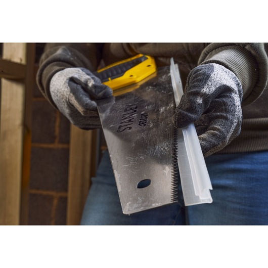 Photo of STANLEY 2-15-288 hand saw held by gloved hands, close-up showing blade and teeth.