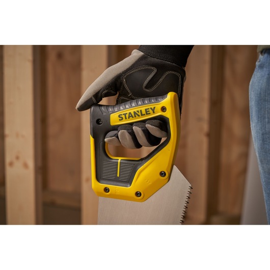 STANLEY 2-15-289 hand saw with yellow and black ergonomic handle, held by gloved hand in workshop.