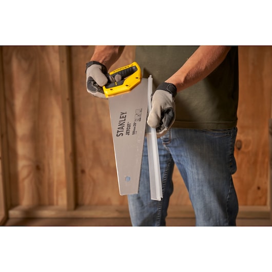 Photo of STANLEY 2-15-599 hand saw cutting metal, with yellow handle and gloves, product in use indoors.