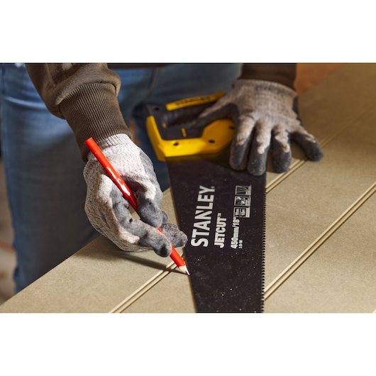 Photo of STANLEY 2-20-180 hand saw held by gloved hands, marking a line on wood with a red pencil.