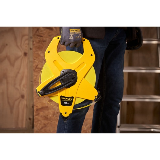 STANLEY 2-34-777 open reel measuring tape held by person wearing gloves, construction site background.