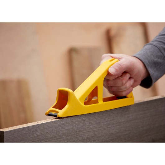 STANLEY 5-21-103 hand rasp tool in yellow, shown smoothing wood surface in close-up photography.