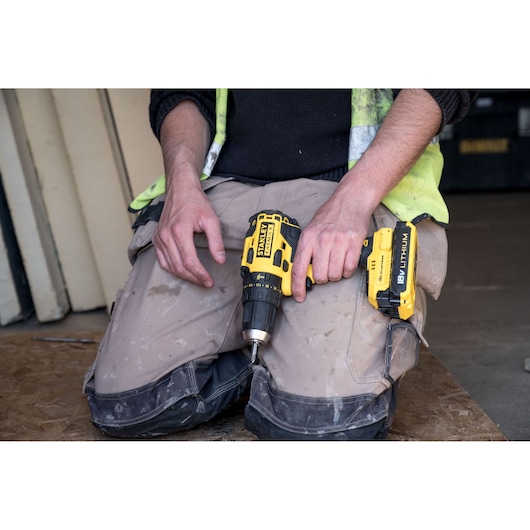 STANLEY FMC627D2 cordless drill driver held by a person in workwear, close-up view.