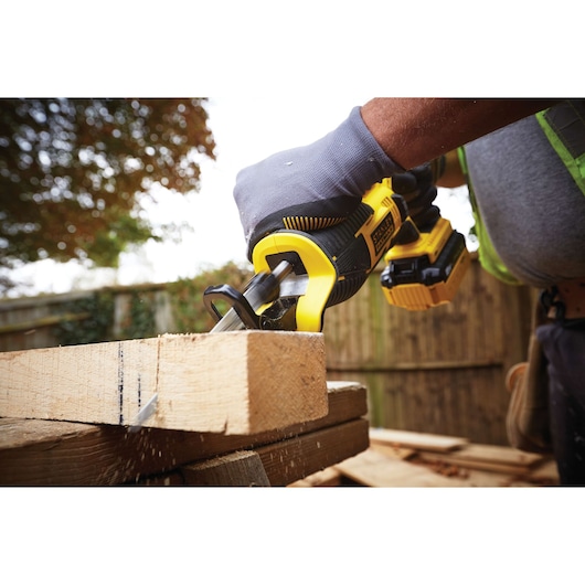 STANLEY FMC675D2 cordless reciprocating saw cutting wood outdoors, close-up of saw and gloved hand.