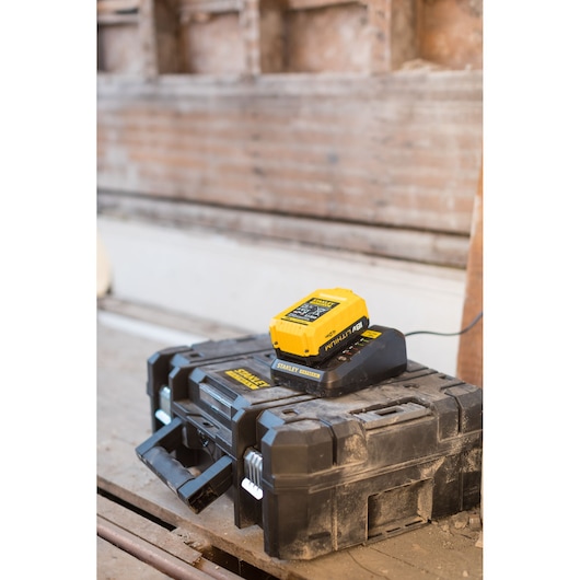 Photo of STANLEY FMC692L black toolbox with yellow battery charger on top, shown in a workshop setting.