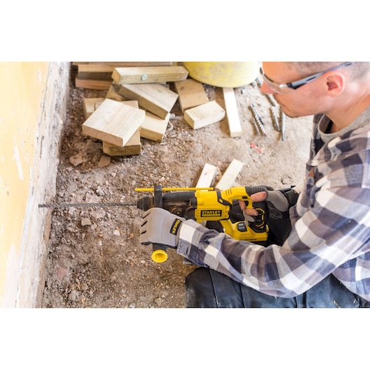 Photo of STANLEY FMCD900B rotary hammer drill in use, drilling into wall, construction site background.